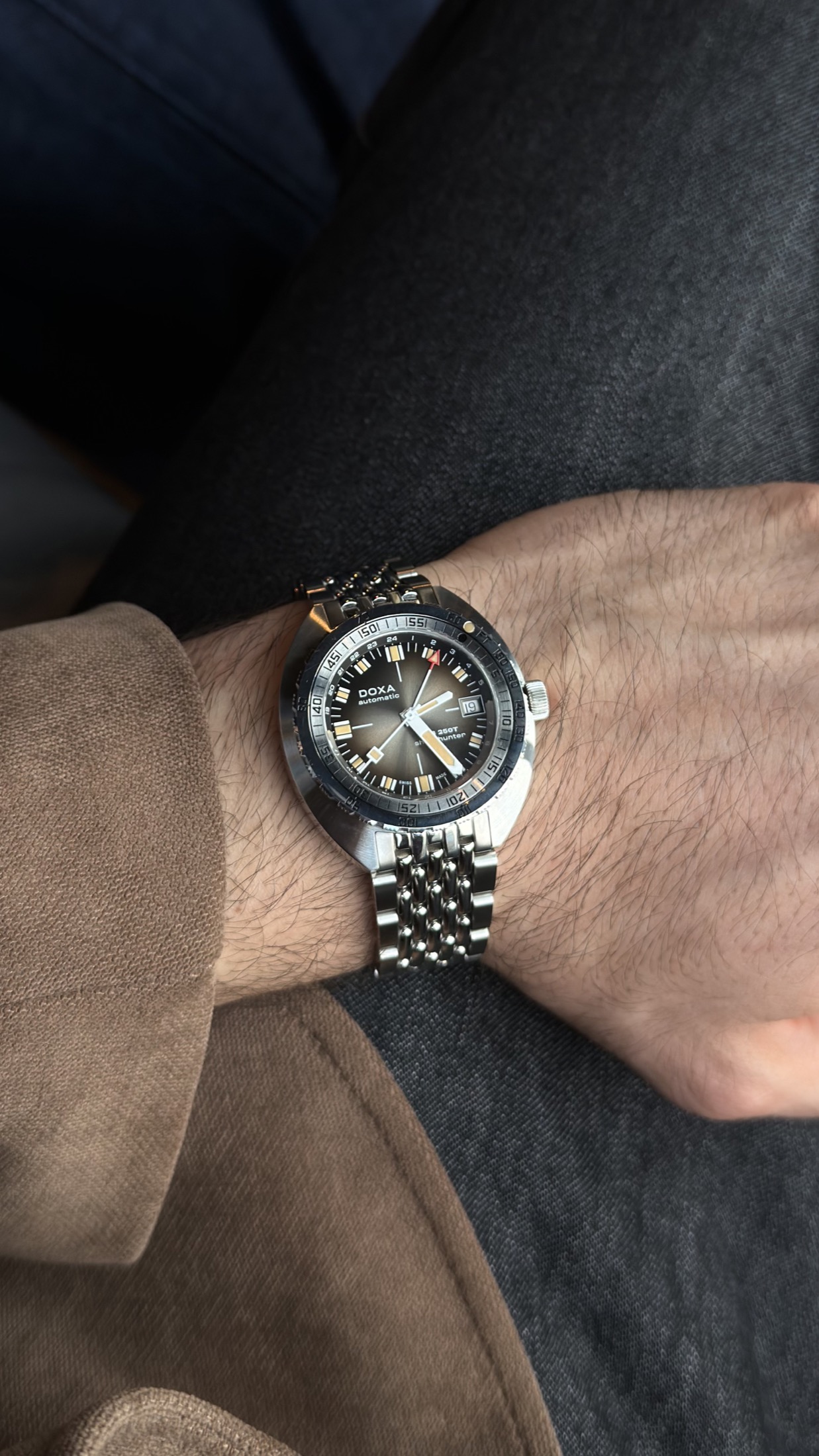 Alperen Aydın’ın bileğinde DOXA SUB 250T GMT Sharkhunter Vintage; kahverengi ceket ve koyu pantolonla